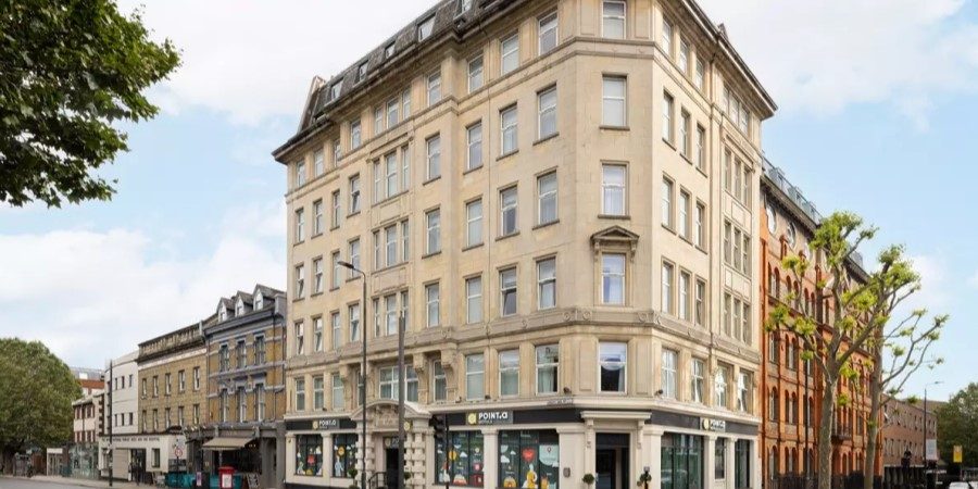 A large building with numerous windows stands prominently along the street, showcasing its modern architectural design.
